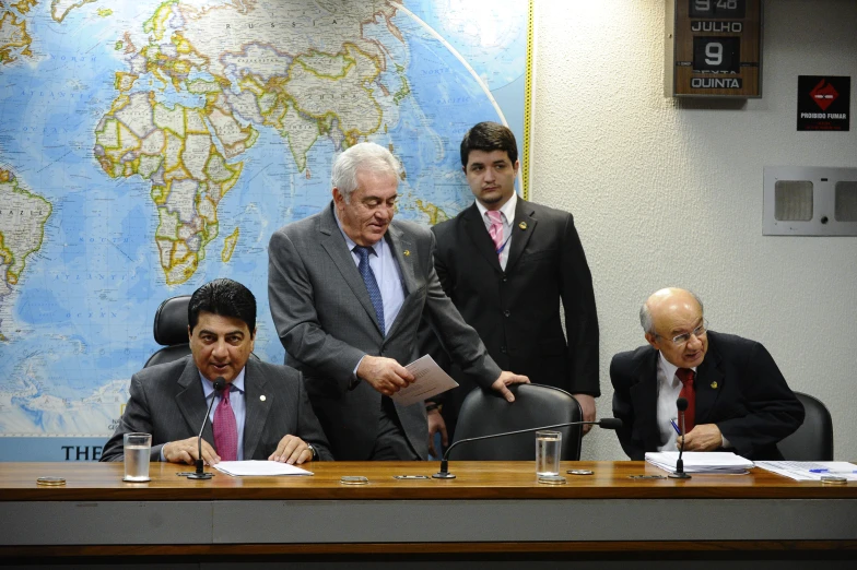 four men wearing suits and ties sitting at a desk