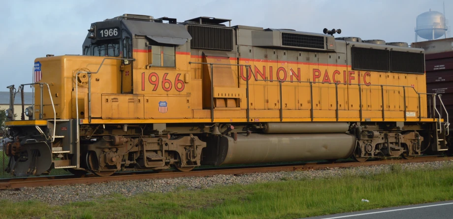 a yellow locomotive on the train tracks by grass