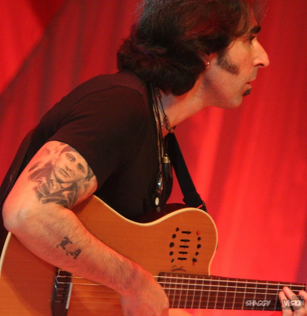 a man with long hair and piercings on holding a guitar