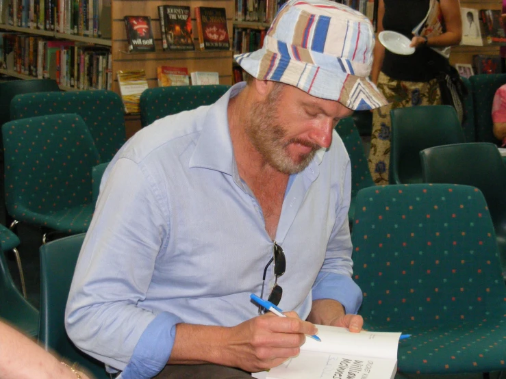 a man sitting on chairs in front of a bookcase with a cap on