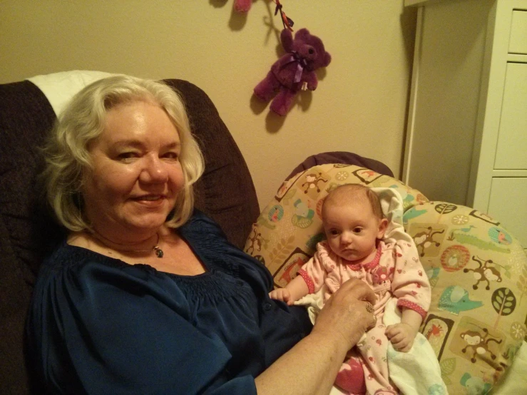 a woman in blue holding a baby in a black chair