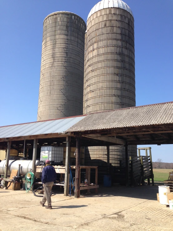 a man walks towards a group of large barrels near a barn