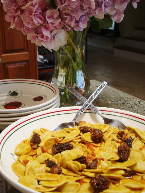 a bowl of pasta, a spoon, and three plates