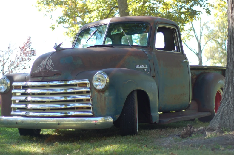 a rusted truck is parked near a tree