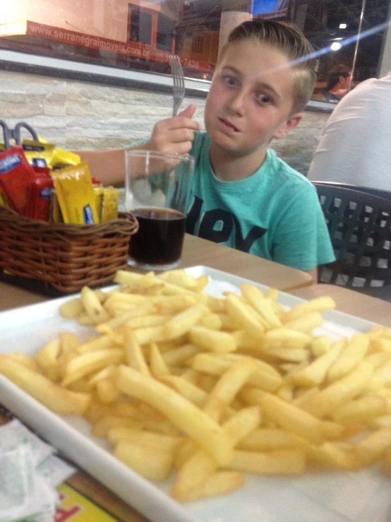 a young man holding up his spoon while sitting at a table with french fries