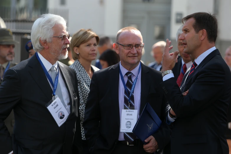 four men in business suits talk and one woman points to the side