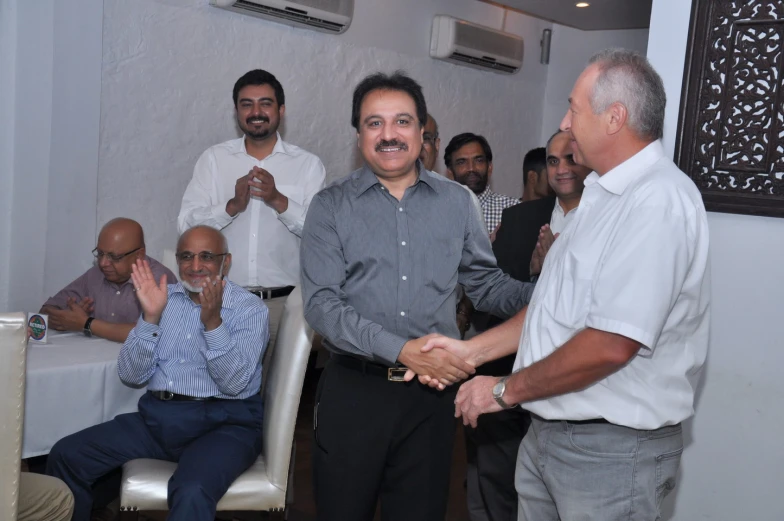 two men shaking hands in front of other people