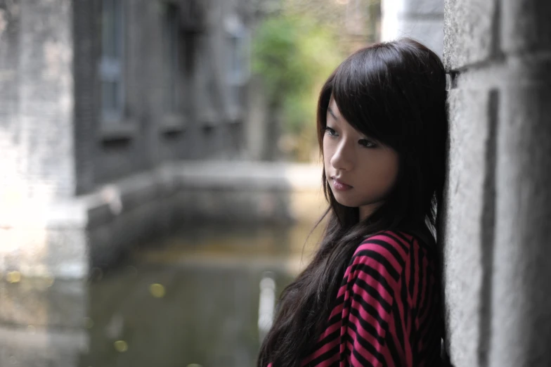 a girl with long black hair leaning against the wall