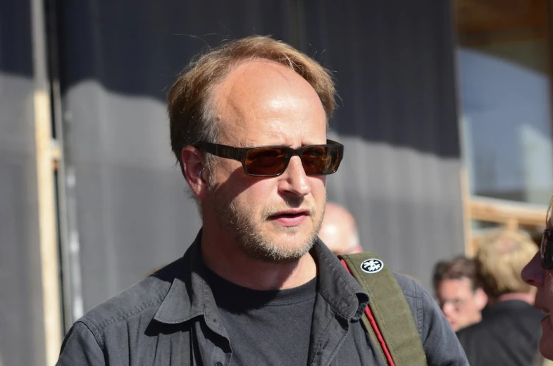 a man in dark shirt talking to another person