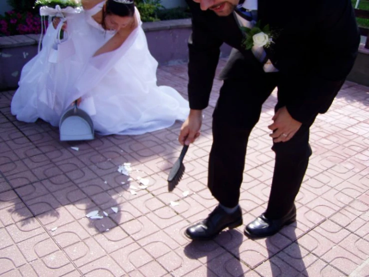 a man with his suit and tie on, and a woman holding a knife behind her and holding flowers