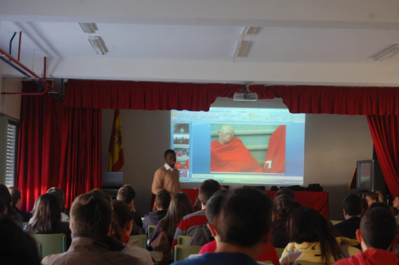 people sitting and standing in chairs watching a presentation on the screen