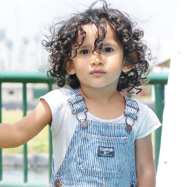 a little girl is outside wearing a blue overall and smiling