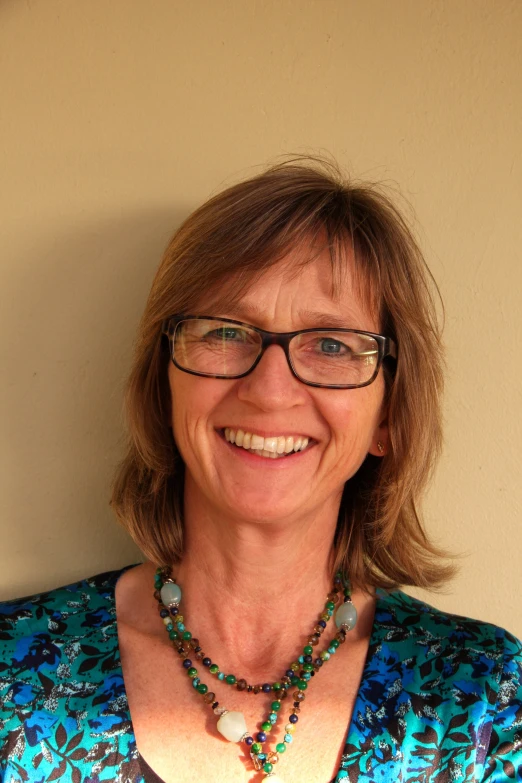 a smiling woman wearing glasses and necklaces