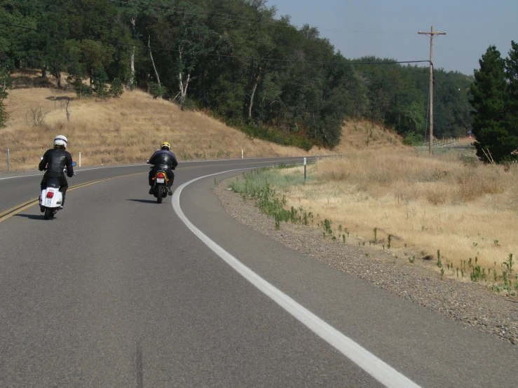 two people on motorcycles driving down a narrow country road