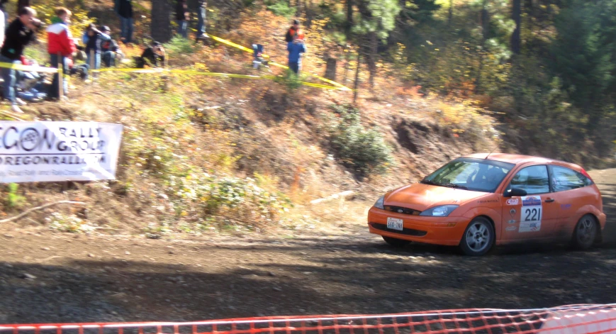 an orange car with number 23 is driving down the road in front of a crowd of people