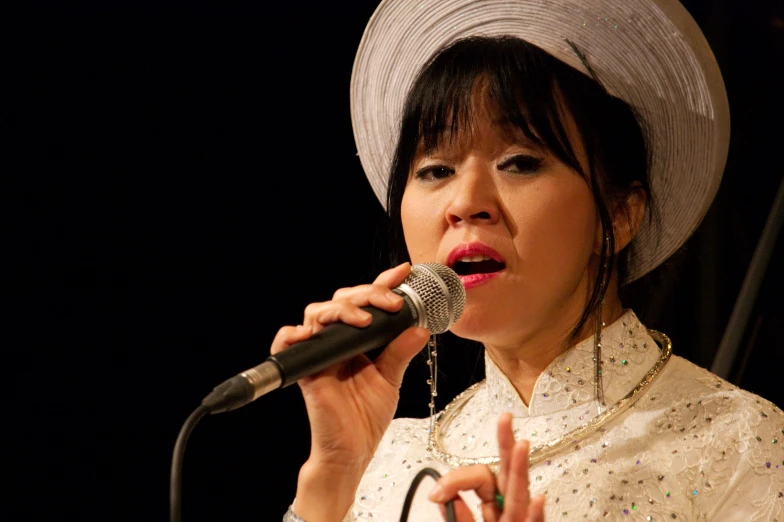 woman with hat on singing into a microphone