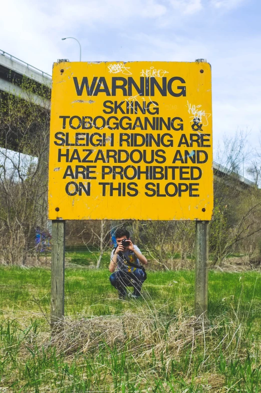 a person taking a po while squatting under a warning sign