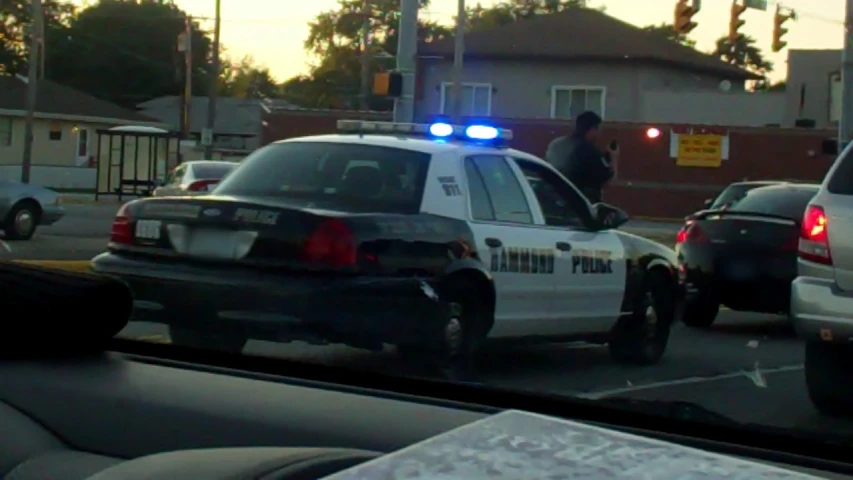 two police cars at an intersection in front of some people