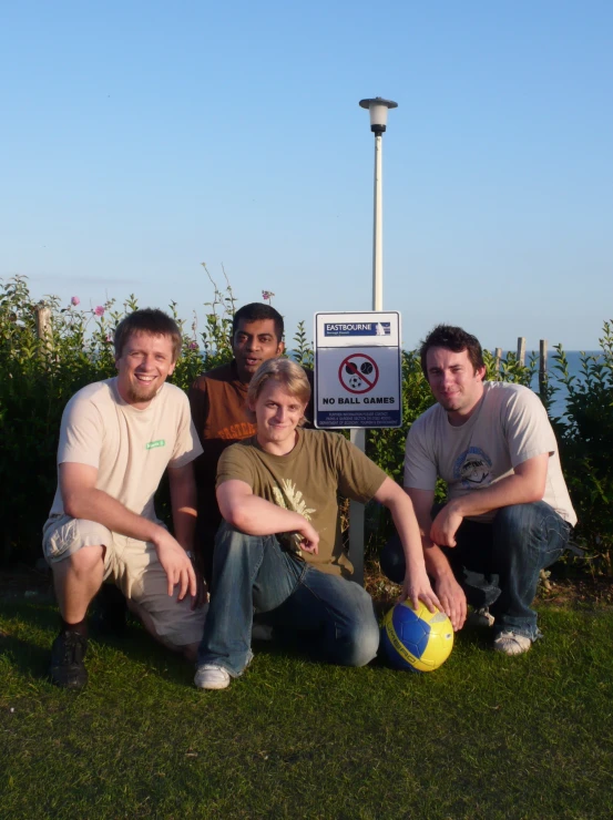 four men posing in front of a no swimming sign