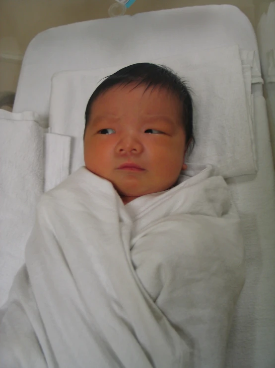 baby wrapped in blanket laying on white bed