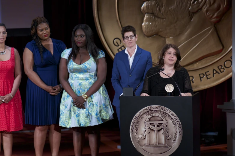 five women and one man stand at a podium