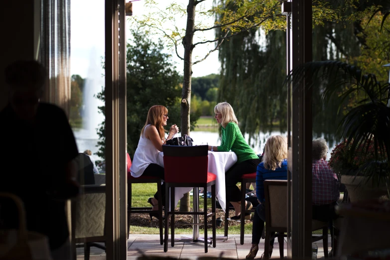 three women sitting at an outside restaurant near water