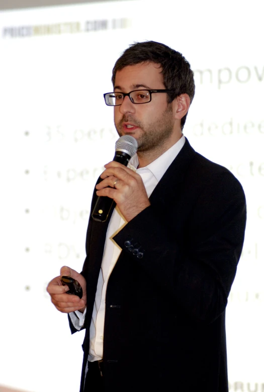 a man in glasses and a black suit holding a microphone