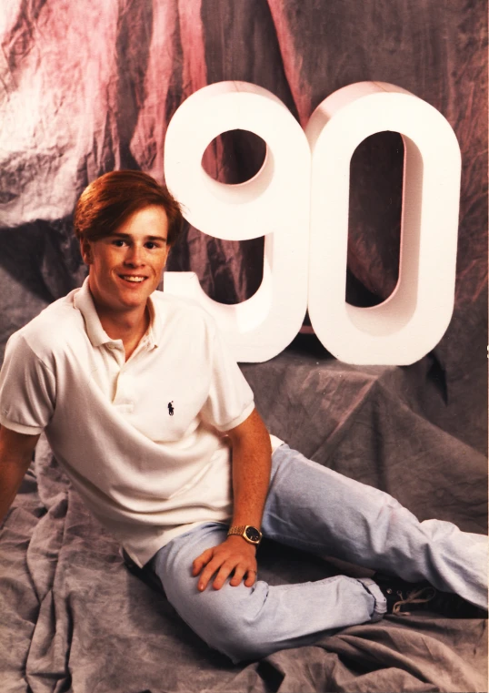 the man is posing in front of a large 90 sign