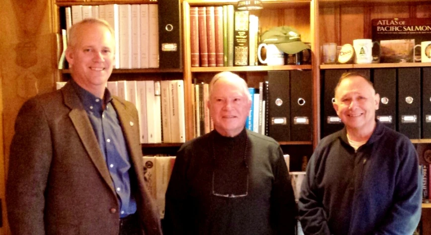 three men in front of a book shelf smiling