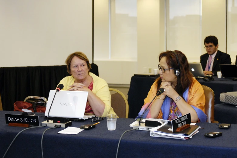 two woman sitting at a table while one is on her phone