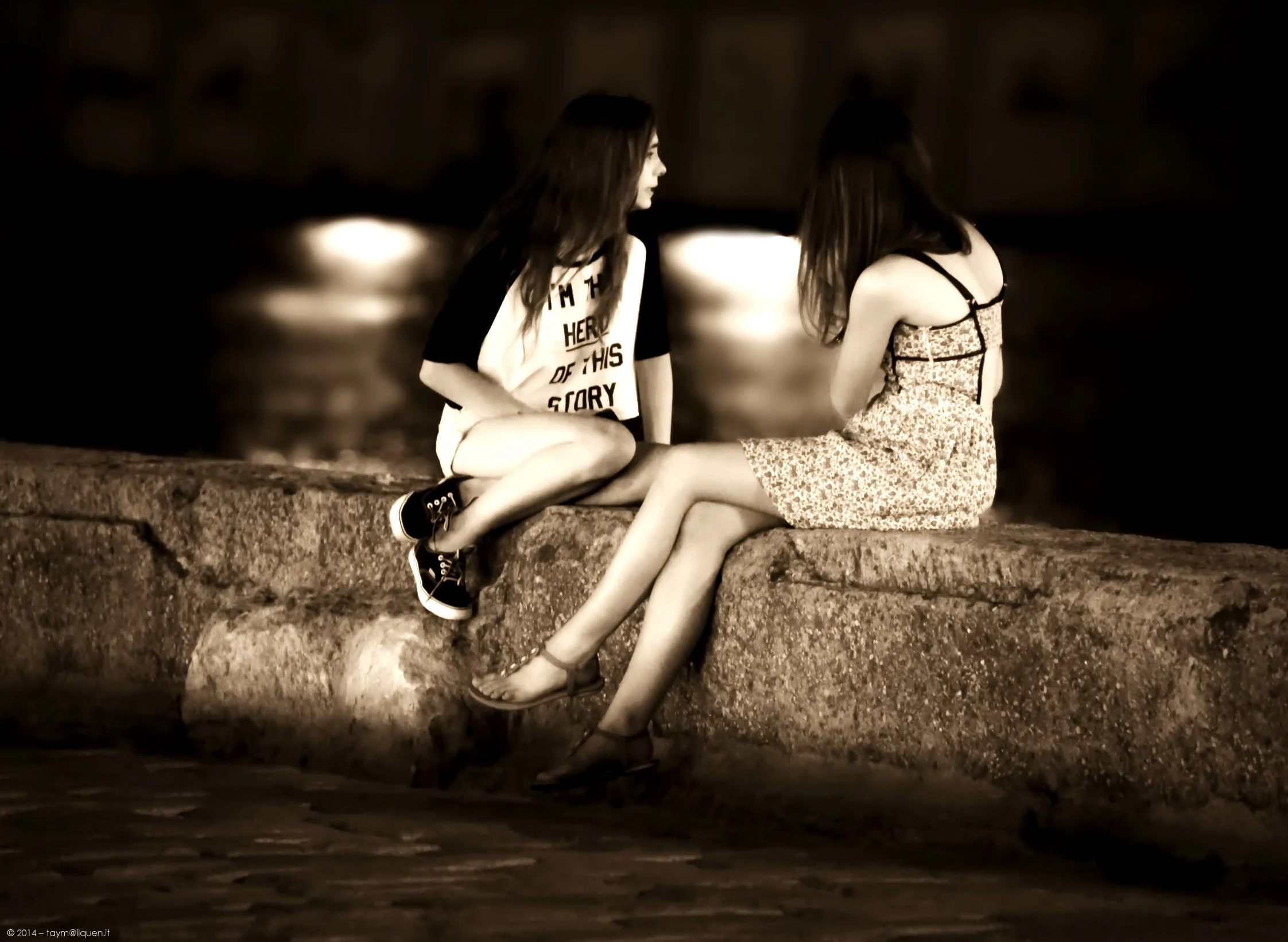 two girls sit on a brick wall next to a lamplight