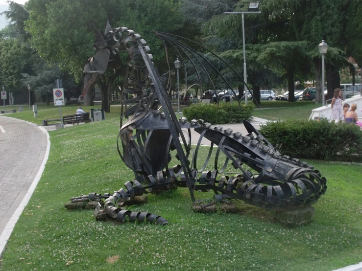 the sculpture of a large insect sits on the grass in front of a street