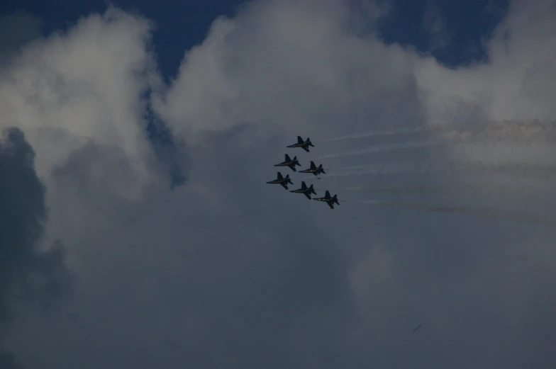 seven airplanes in a formation flying under clouds