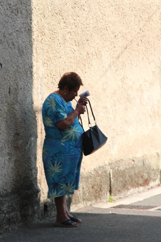 a woman in a blue dress is holding a bag and looking at her phone