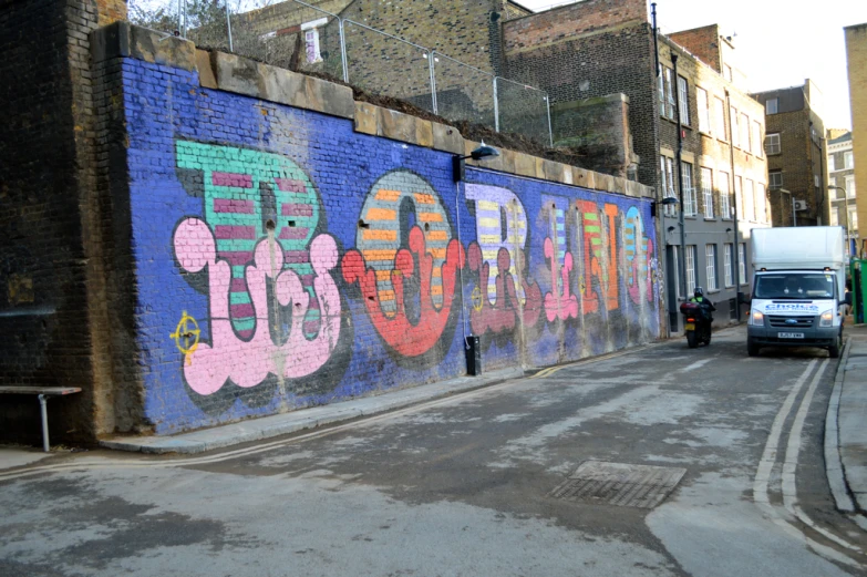 a very large and colorful graffiti covered wall next to a sidewalk