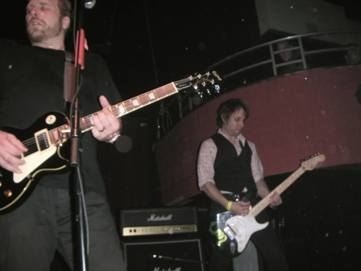 two men playing guitars and one is singing into the microphone