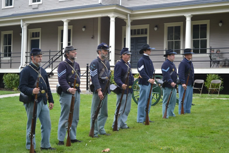 several men dressed in civil war reenactment uniforms, standing on the lawn