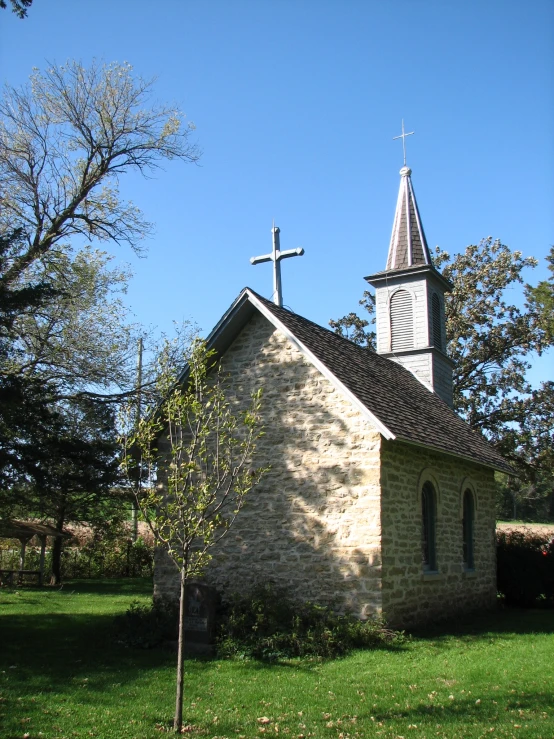 a small old church with steeple, tree, and crosses on top