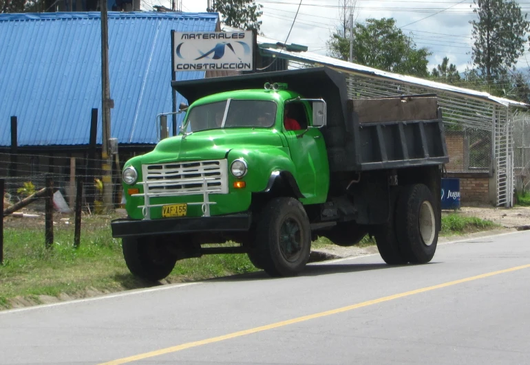 a green truck drives down the road past a blue building