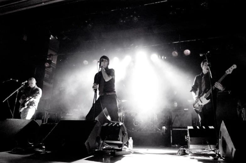 three male band performing on stage under spotlights