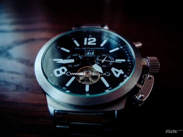 a black and silver watch sitting on top of a wooden table