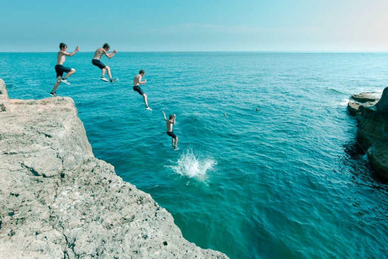 a group of people jumping from rocks off the shore into the water