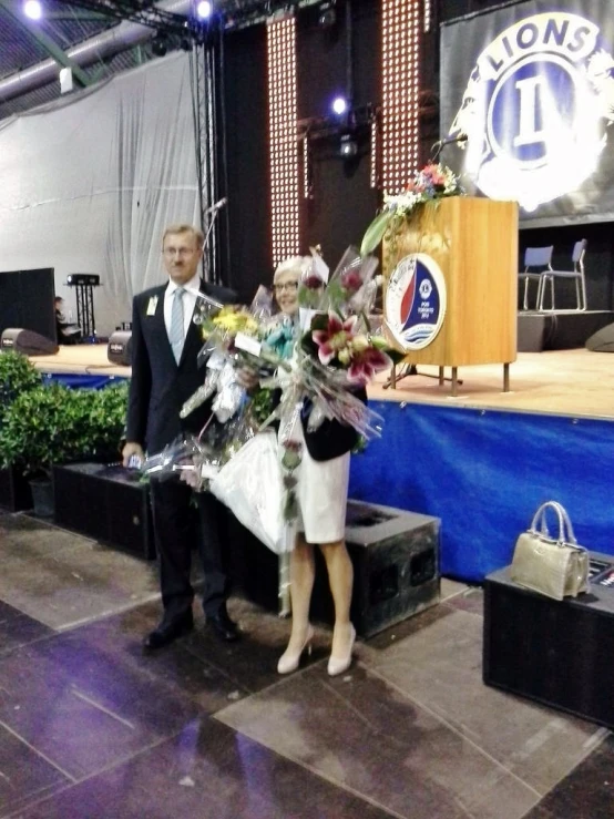 the man and woman are posing with flowers in front of a screen