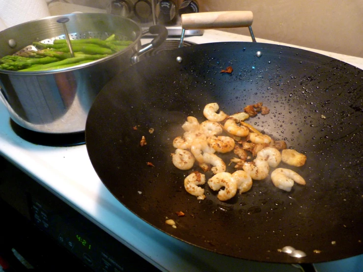 two pans sit on top of the stove cooking shrimp