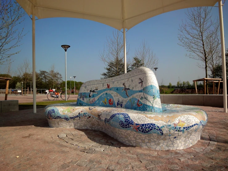 a cement bench sits under an umbrella on top of a brick surface