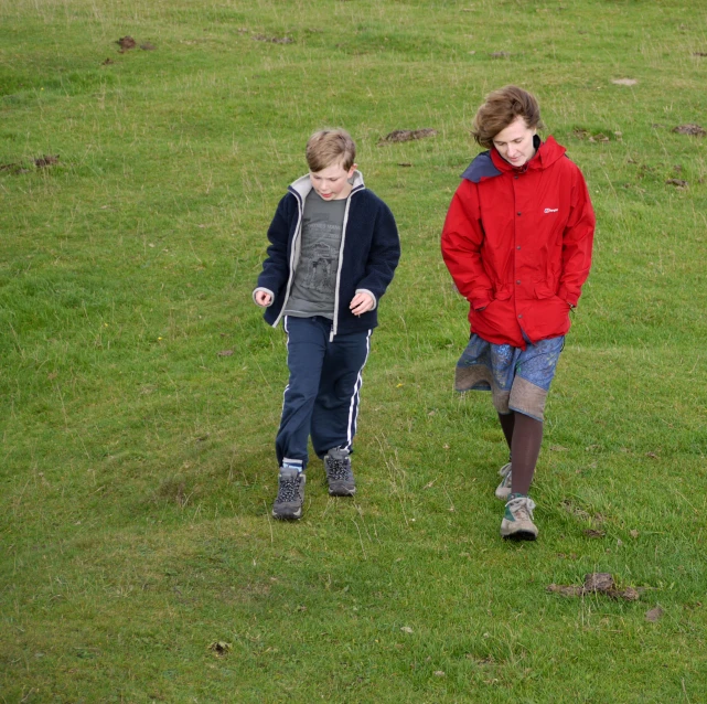 two children walking through an open field holding a red frisbee