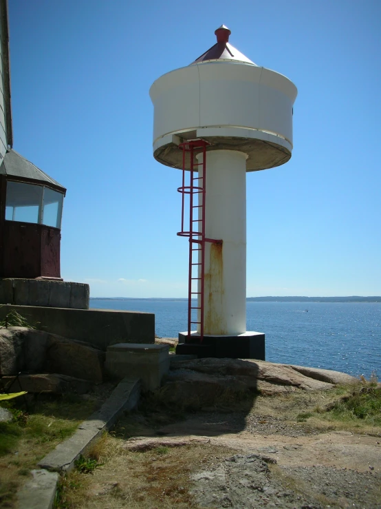 a large white tower in the grass next to some water