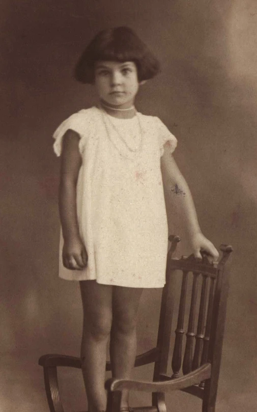 a girl in dress on rocking chair wearing a hat