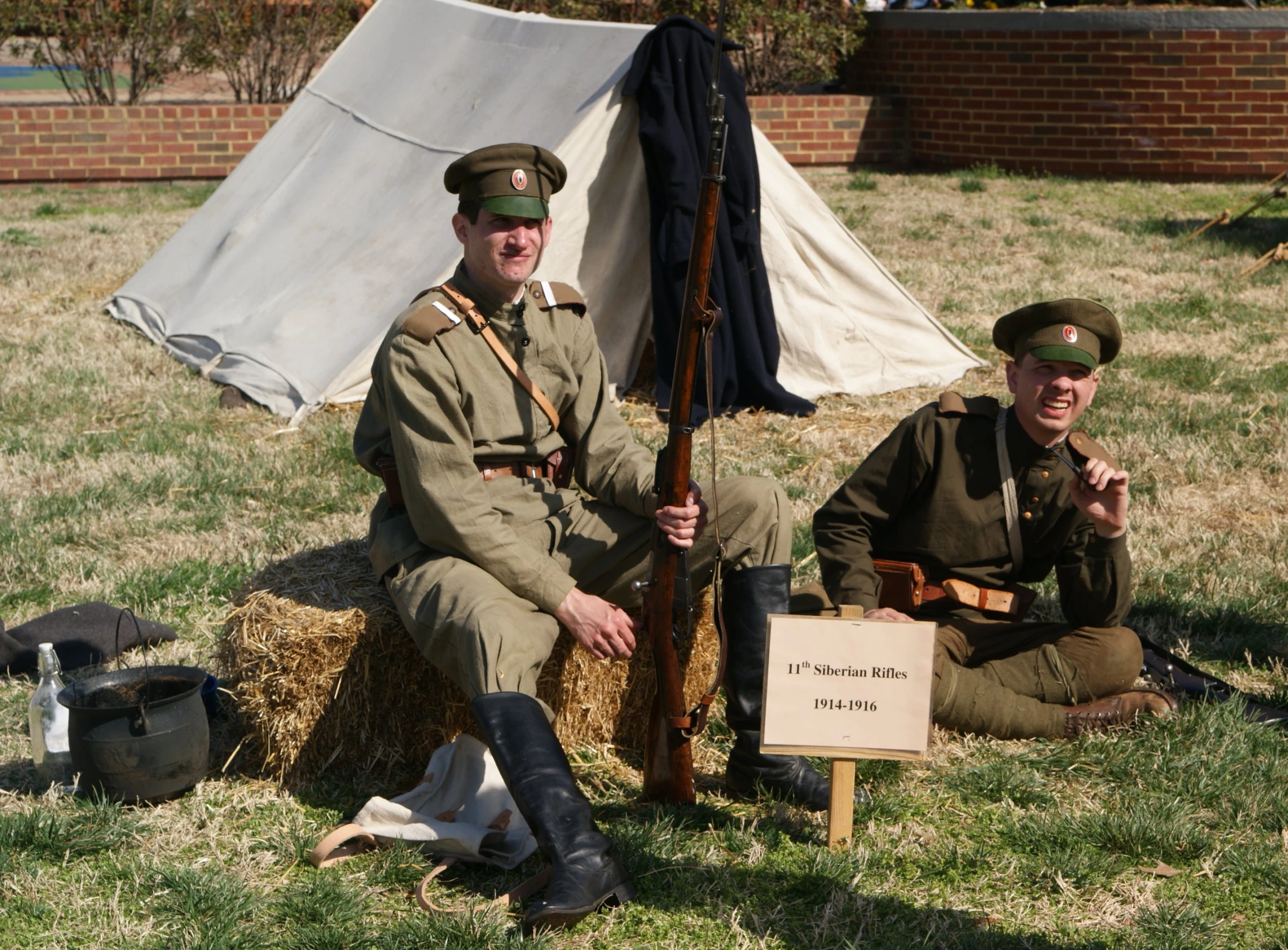 two soldiers sitting in a field with a white tent