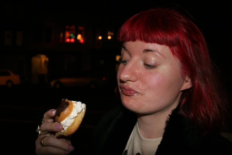 a woman with red hair holding a donut with white frosting